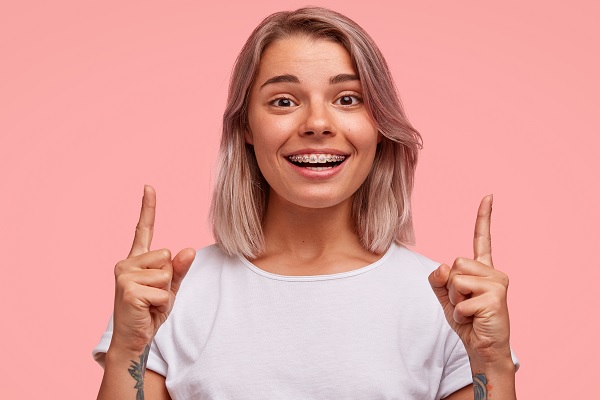 mujer joven sonríe con correctores en sus dientes, mostrando una perfecta higiene, en un fondo rosa