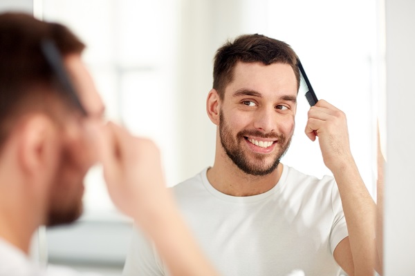 Trasplante capilar - hombre joven peinando su cabello frente al espejo, que demostrando el cuidado correcto del cabello y el trasplante de cabello