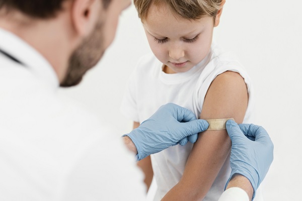 medico aplicando una tira adhesiva sanitaria a niño luego de vacunarlo, posiblemente contra esta enfermedad