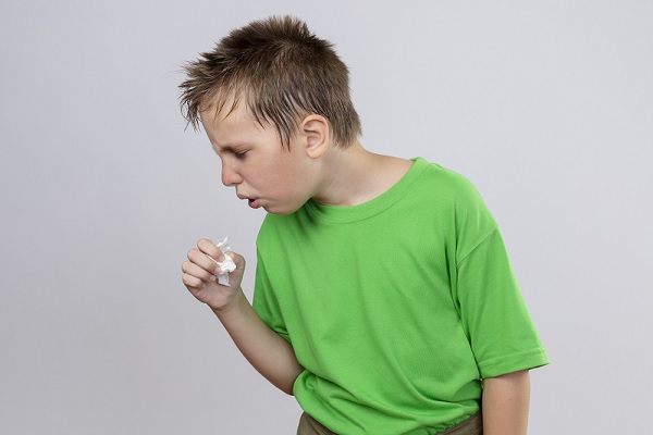 historia natural de la tosferina, un niño de camisa verde tosiendo tratando de taparse la boca con la mano