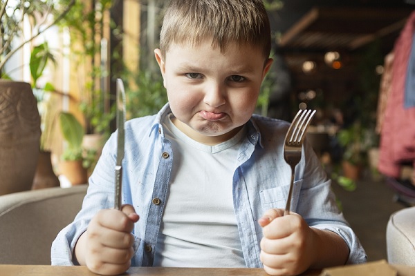 síndrome metabólico en niños, un niño con un gesto de molestia en su cara, sosteniendo cubiertos en sus manos