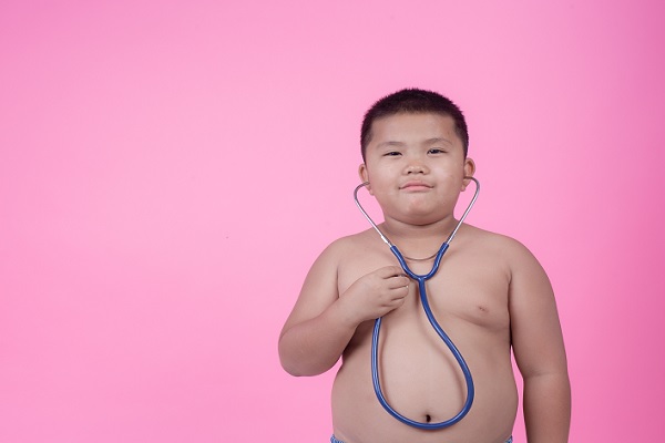 un niño sin camisa y con grasa abdominal, tiene un estetoscopio en sus oídos escuchando los latidos de su corazón