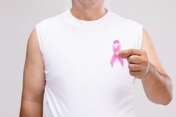 cáncer de mama en hombres - hombre sostiene la cinta rosa del cáncer de mama en su mano