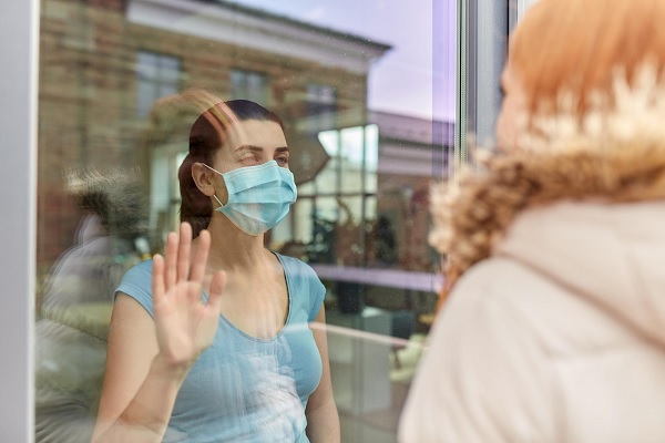 un mujer con enfermedad viral usa mascarilla y habla con su amiga a través del cristal de una casa para prevenir la propagación de la enfermedad