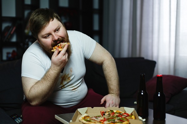 enfermedades más comunes en México - un hombre con obesidad come pizza y bebe cerveza que contribuye negativamente a su condición 